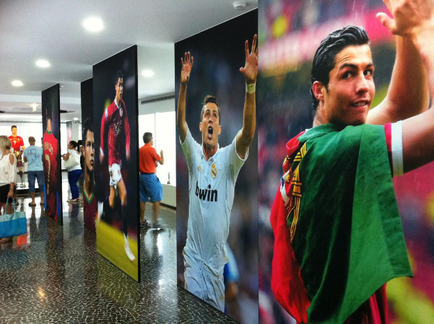 Ein Banner mit dem Fußballspieler Rolando, mit Menschen, die links neben einem Tisch stehen und Lichter oben.