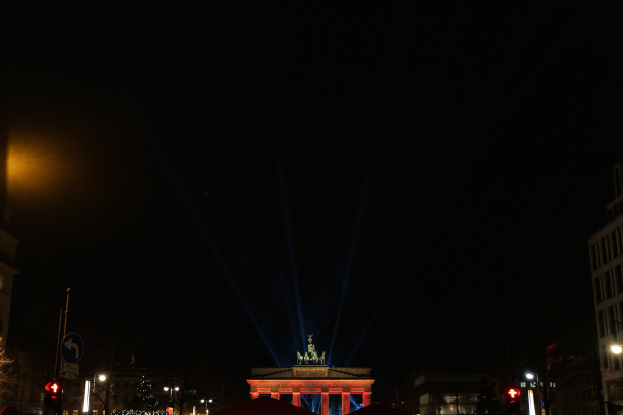 Brandenburger Tor bei Nacht, beleuchtet von Straßenlaternen, umgeben von Gebäuden, Bäumen, Pfählen, Verkehrszeichen, Schildern und Zelten unter einem dunklen Himmel.