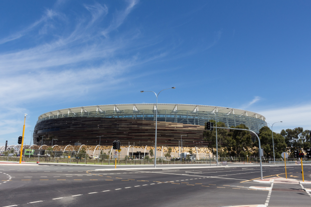 Großer Stadion mit starkem Verkehr davor, umgeben von Straßeninfrastruktur und Bäumen unter einem bewölkten Himmel.