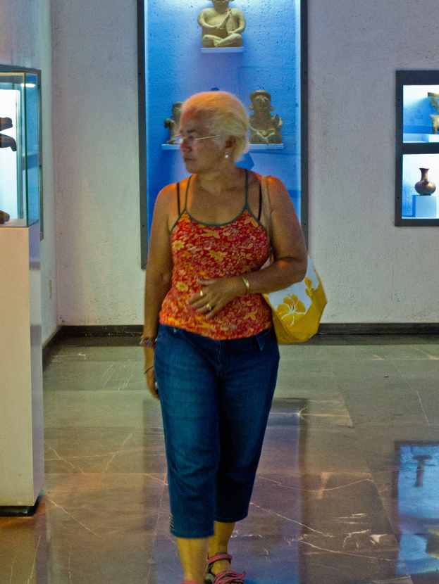 Eine Frau mit einer Handtasche steht vor einer Wand mit Foto Rahmen und Statuen.