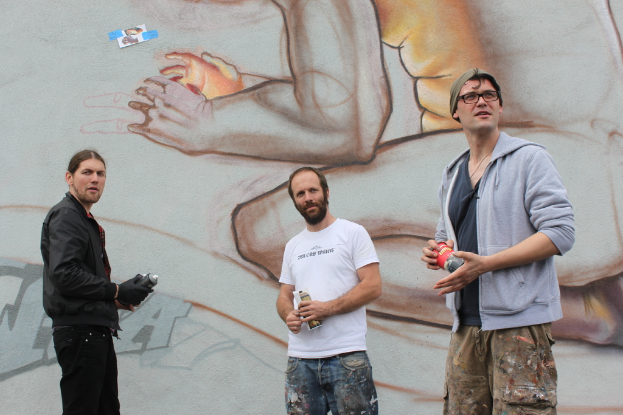 Menschen mit Farbspr√∂hflaschen in der Hand, mit Graffiti an der Wand dahinter.