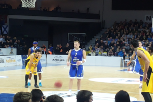 Eine Gruppe von Männern in blauen und gelben Uniformen spielt Basketball auf einem Court, umgeben von einer Menge im Publikum, mit einem Basketballkorb und einer Wand im Hintergrund, während des 7days Eurocup Regular Season Round 2 Spiels zwischen Fenerbahce und Real Madrid.