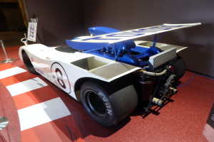 Ein weiß-blauer Rennwagen in einem Museum ausgestellt, umgeben von Absperrungen und Infotafeln, mit einer Wand im Hintergrund, die auf das Goodwood Festival of Speed hindeutet.