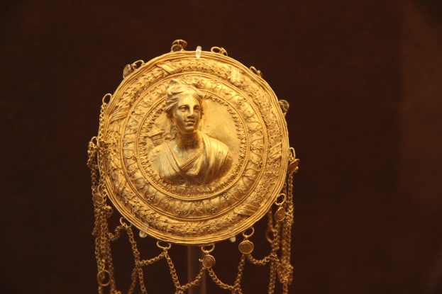 Goldene Medaille mit einer Frauengestalt auf dunklem Hintergrund, mit feiner Verzierung und einem majestätischen Erscheinungsbild.