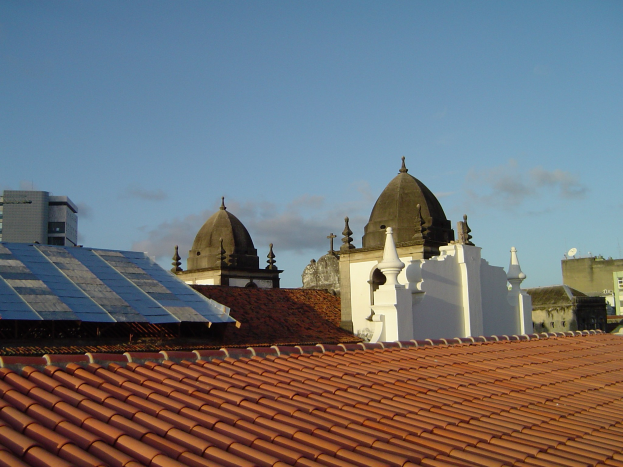 Stadtlandschaft mit mehreren Gebäuden im Vordergrund, einem klaren blauen Himmel im Hintergrund und Solarpanels auf dem Dach eines Gebäudes.