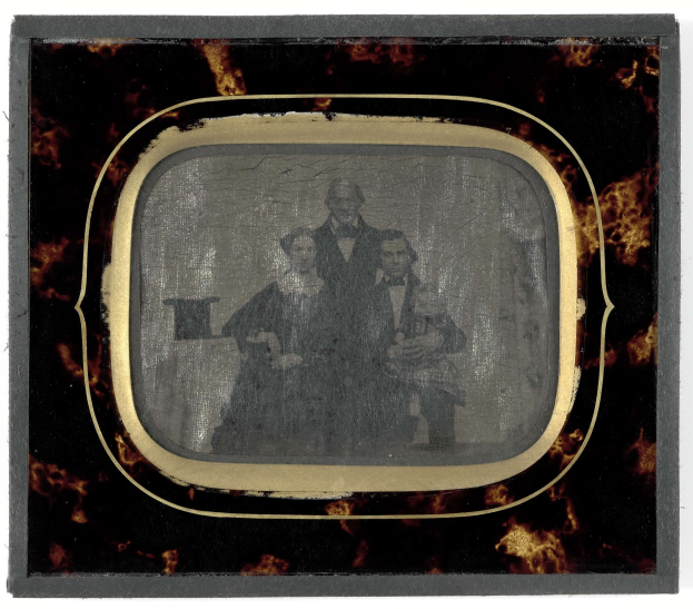 Schwarzes-Weiß-Foto eines Mannes in Anzug und Krawatte und einer Frau in unbekannter Kleidung, die vor einem Fernseher stehen und ernst aussehen.