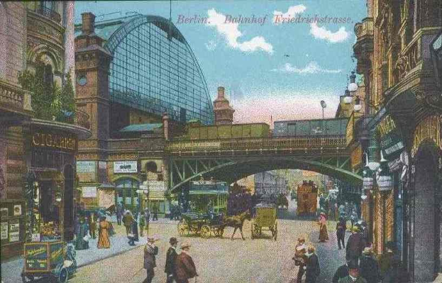 Alte Postkarte einer belebten Berliner Straße mit Pferdewagen, Fußgängern, Gebäuden, einer Brücke und Wolken im Hintergrund, mit Text oben.