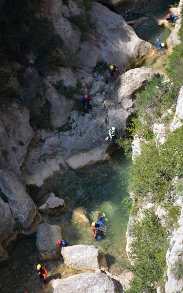 Eine Gruppe von Menschen in Helmen, die eine felsige Klippe umgeben von Wasser, Felsen, Pflanzen und Bäumen hochklettern.