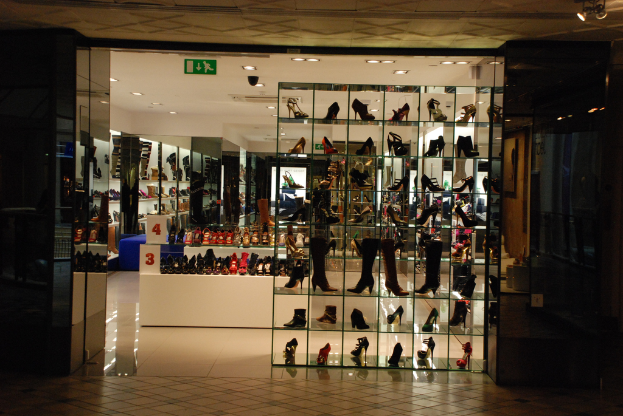 Eine Auswahl verschiedener Schuhe und Sandalen auf einem weißen Tisch in einem Schuhgeschäft, mit einer Wand auf der linken Seite und der Decke oben.