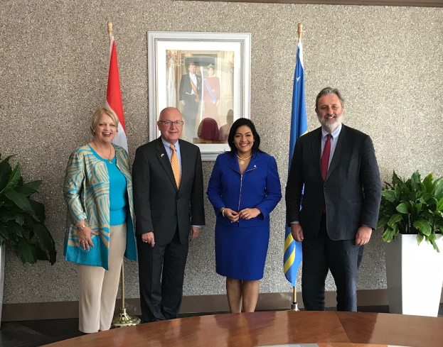 Gruppe von Menschen, die um einen Tisch mit Papieren stehen, umgeben von Fahnen, Topfpflanzen und einem Rahmenfoto an der Wand, was auf eine Unterzeichnung eines U.S.-Kanada-Vertrages hindeutet.