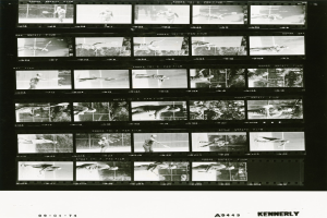 Schwarzes und weißes Foto eines Mannes in einem weißen Hemd und Shorts beim Tennis spielen, der einen Schläger in der rechten Hand hält, mit einem Filmstreifen im Hintergrund.