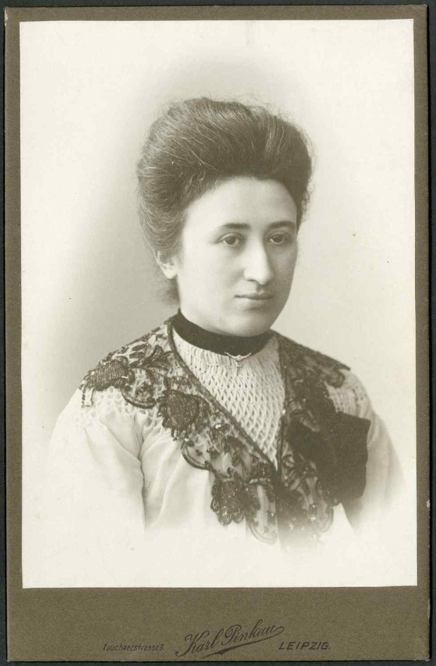 Schwarz-weißes Foto einer Frau in einem weißen Kleid mit einem gemusterten Schultertuch, identifiziert als Karl Pinkau Leipzig, die direkt in die Kamera schaut.