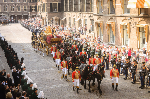 Eine Gruppe von Menschen, die auf Pferden eine Straße entlangreiten, neben einer Menge mit Kameras und Handys, mit Gebäuden und Laternen im Hintergrund während der königlichen Hochzeit von König Willem-Alexander und Königin Maxima der Niederlande.