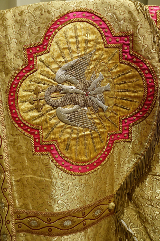 Nahaufnahme eines Priestergewandes mit goldener und roter Stickerei vor einer Wand als Hintergrund, mit detaillierter und luxuriöser Verarbeitung.