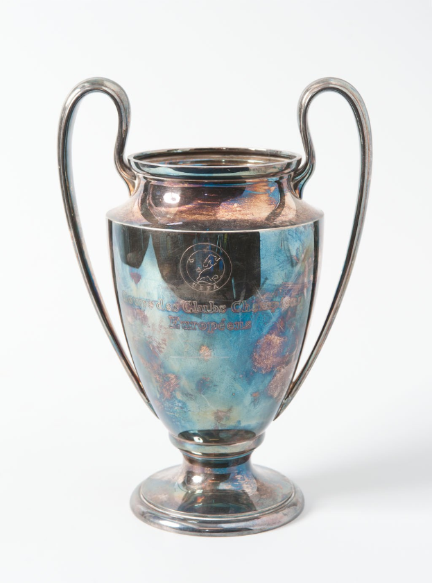 UEFA Champions League-Trophäe, ein stählerner Pokal mit zwei Griffen, blau und silbern, mit der Inschrift "UEFA Champions League" auf einem weißen Hintergrund.