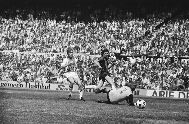 Schwarzes und weißes Foto von Fußballspielern in Aktion auf einem Feld mit Zuschauern im Hintergrund und einer Bundesliga 1978-79 Ajax 1-1 Hannover 96-Banner.