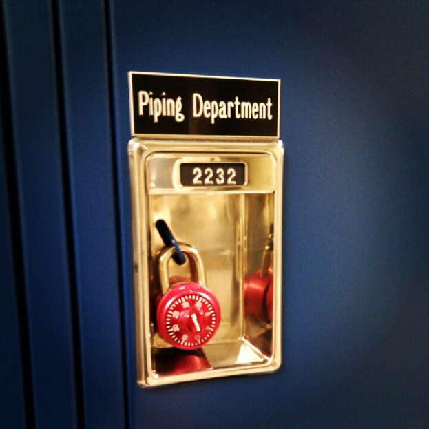 Ein blauer Spind mit einem roten Vorhängeschloss und einer Namensschild mit der Aufschrift "Rohrleitungsabteilung".